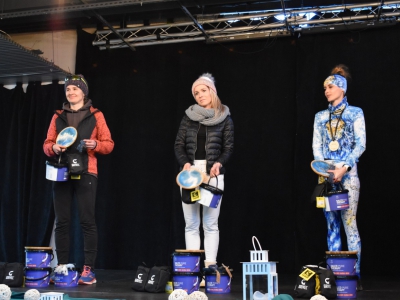 Trzy kobiety w strojach sportowych stoją na scenie. Pozują do zdjęcia z nagrodami.